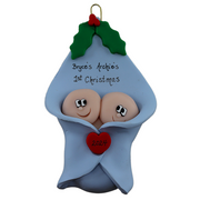Ornament with twin infant heads poking out of a blue baby blanket, personalized with names.