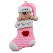 Ornament with infant head in a pink hat poking out of a pink stocking, personalized with name.
