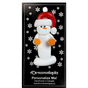 Ornament of white snowman in red hat holding orange cheerleader pom-poms, on display backing card.