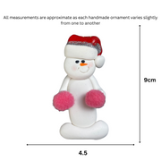 Ornament of white snowman in red hat holding pink cheerleader pom-poms, graphed to show size (4.5x9cm).