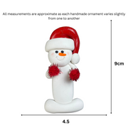 Ornament of white snowman in red hat holding red cheerleader pom-poms, graphed to show size (4.5x9cm).