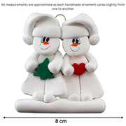 Family ornament with 2 white snowmen in hats, holding holiday objects, graphed to show size (8cm).