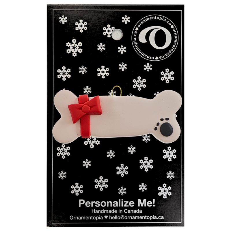 Ornament of dog bone with ribbon and paw print, on display backing card.