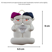 A couple’s ornament of two white snowmen holding a plastic diamond, graphed to show size (6.5x9cm).