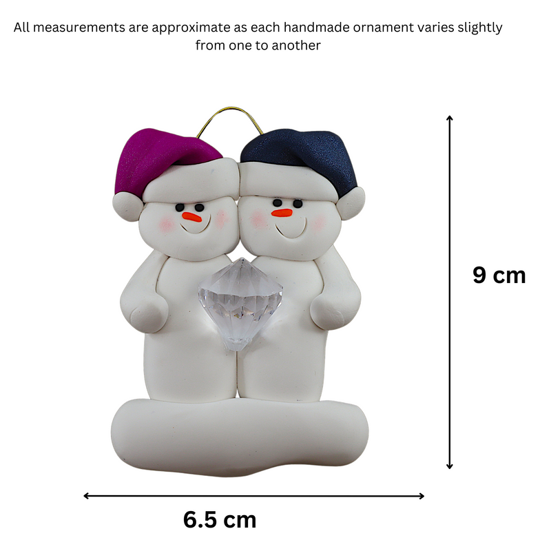 A couple’s ornament of two white snowmen holding a plastic diamond, graphed to show size (6.5x9cm).