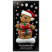 Tan bear in red festive hat holding colourful present ornament, on display backing card.