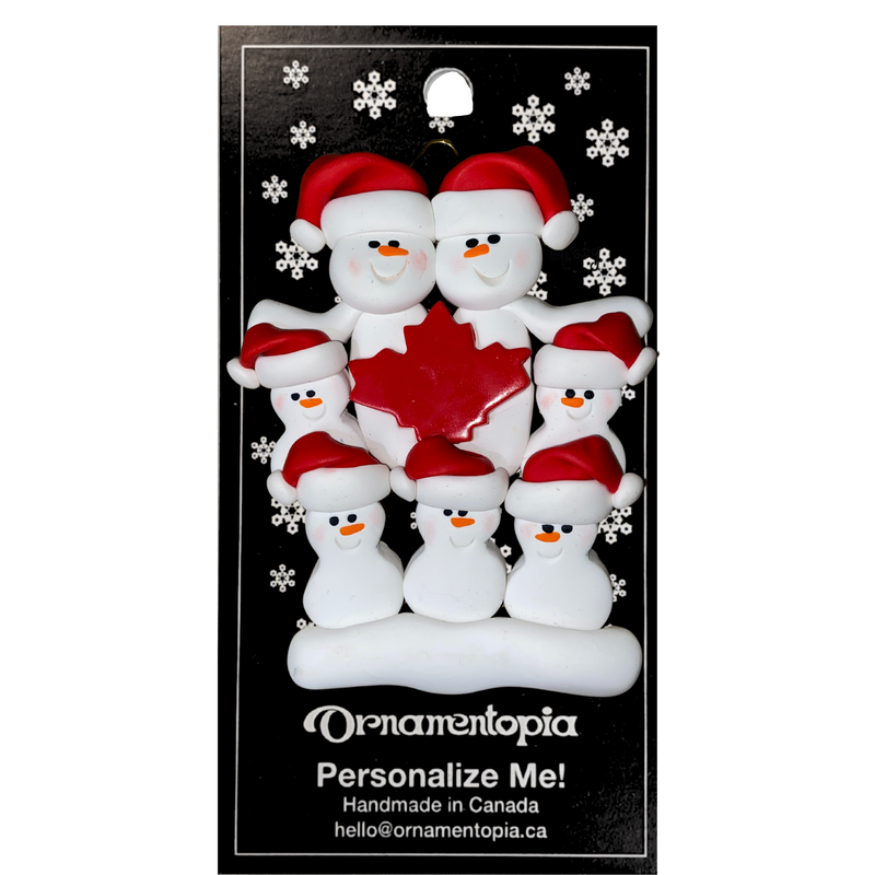 Family ornament with 7 white snowmen in red hats, gathered around a red maple leaf, on display backing card.