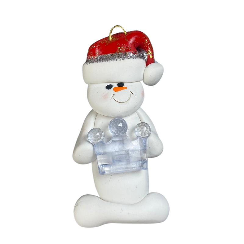 Ornament of white snowman in red hat holding clear plastic crown.