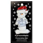 Ornament of white snowman in red hat holding clear plastic crown, on display backing card.