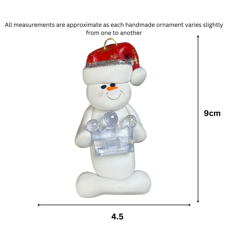 Ornament of white snowman in red hat holding clear plastic crown, graphed to show size (4.5x9cm).