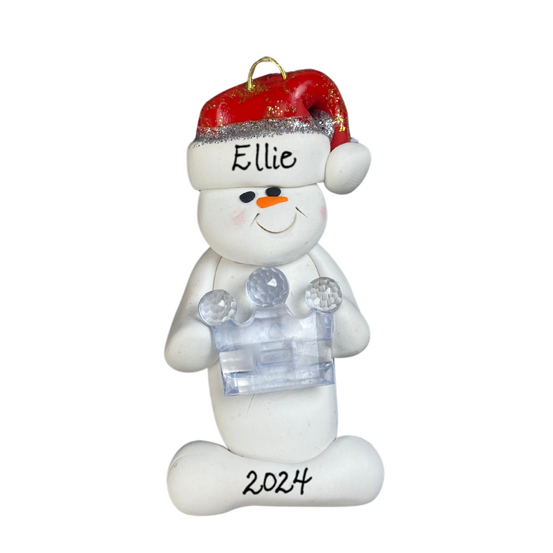 Ornament of white snowman in red hat holding clear plastic crown, personalized with name.