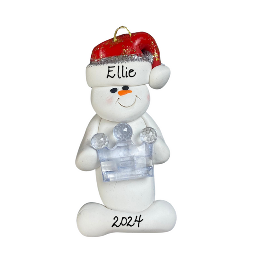Ornament of white snowman in red hat holding clear plastic crown, personalized with name.
