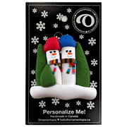 Family ornament with 2 snowmen in colourful scarves and hats, hemmed by Christmas trees, on backing card.