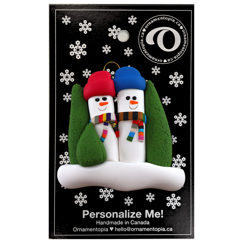 Family ornament with 2 snowmen in colourful scarves and hats, hemmed by Christmas trees, on backing card.