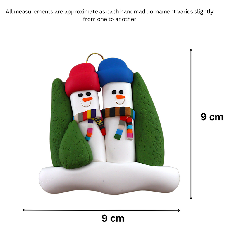 Family ornament with 2 snowmen in colourful scarves and hats, hemmed by Christmas trees, graphed to show size (9x9cm).