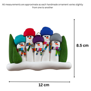 Family ornament with 5 snowmen in colourful scarves, hemmed by Christmas trees, graphed to show size (12x8.5cm).