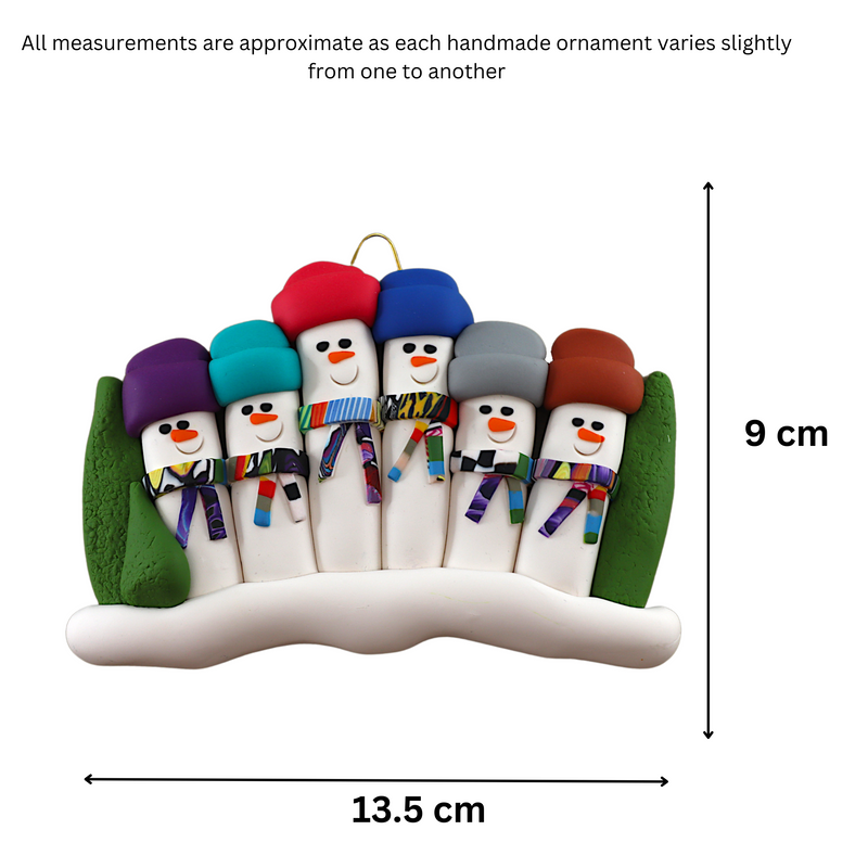Family ornament with 6 snowmen in colourful scarves and hats, hemmed by Christmas trees, graphed to show size (13.5x9cm).