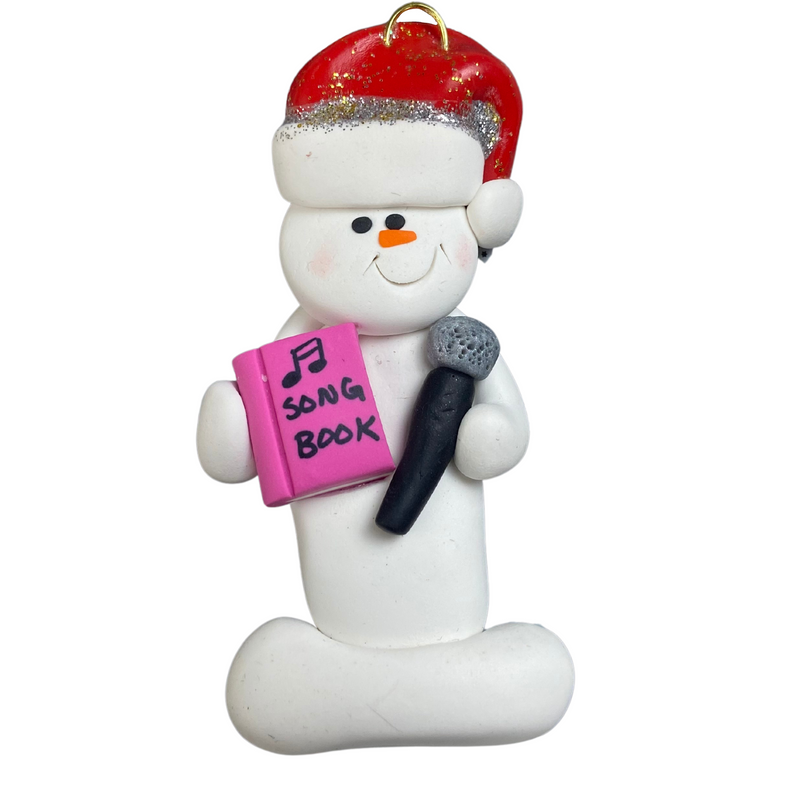 Ornament of white snowman in red hat holding a microphone and pink music book.