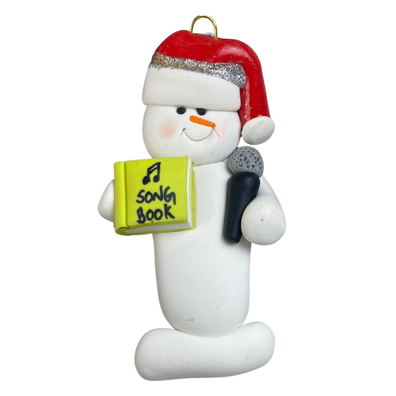 Ornament of white snowman in red hat holding a microphone and green music book.