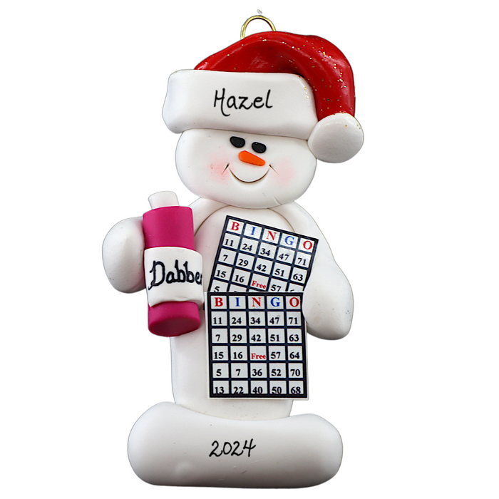 Ornament of white snowman in red hat holding a bingo card and dabber, personalized with name.