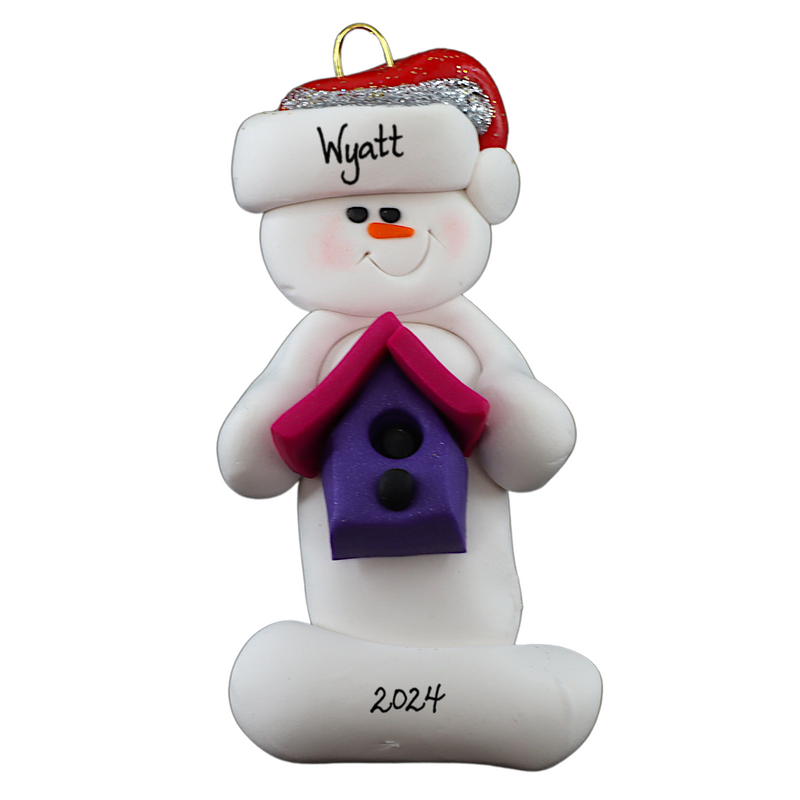 Ornament of white snowman in red hat holding a pink and purple birdhouse, personalized with name.