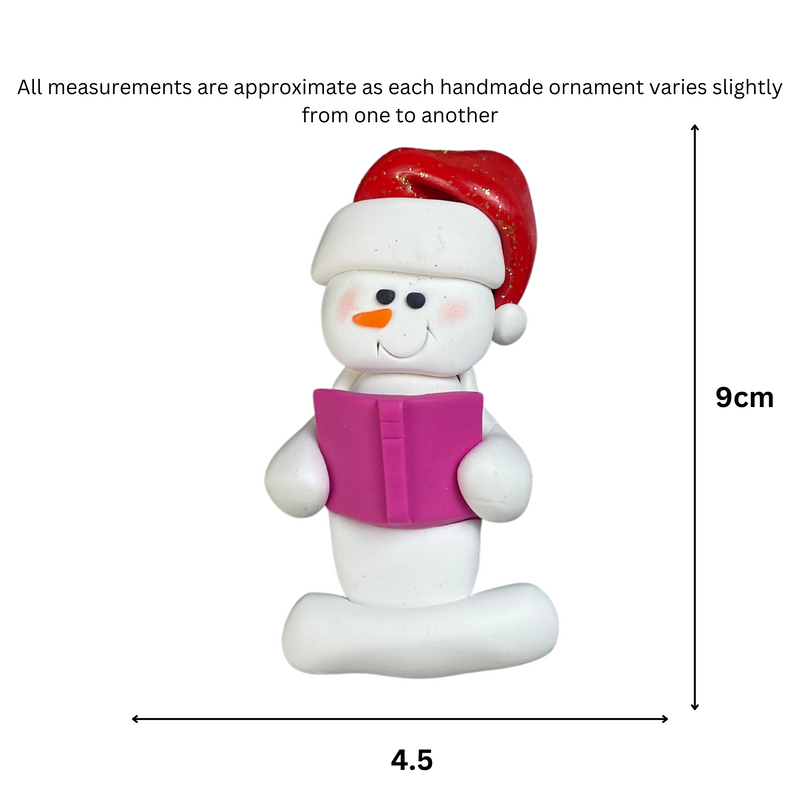 Ornament of white snowman in red hat holding a pink book, graphed to show size (4.5x9cm).