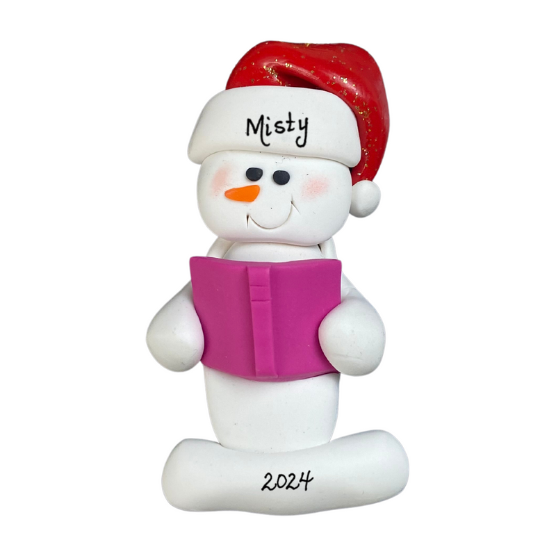 Ornament of white snowman in red hat holding a pink book, personalized with name.