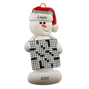 Ornament of white snowman in red hat holding large crossword puzzle, personalized with name.