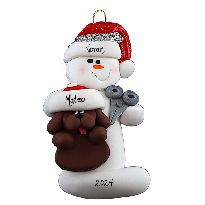 Ornament of white snowman in red hat holding a brown dog and a pair of scissors, personalized with name.