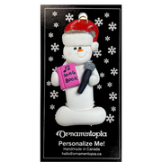 Ornament of white snowman in red hat holding a microphone and pink music book, on display backing card.