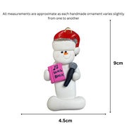 Ornament of white snowman in red hat holding a microphone and pink music book, graphed to show size (4.5x9cm).