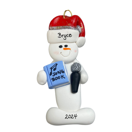 Ornament of white snowman in red hat holding a microphone and blue music book, personalized with name.
