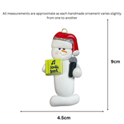 Ornament of white snowman in red hat holding a microphone and green music book, graphed to show size (4.5x9cm).