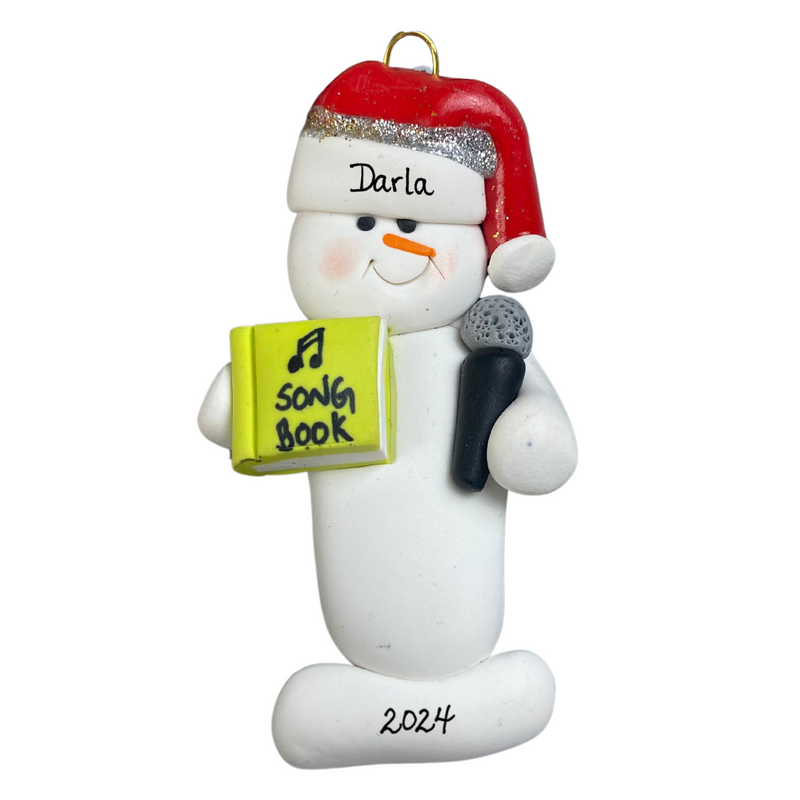 Ornament of white snowman in red hat holding a microphone and green music book, personalized with name.