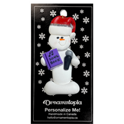 Ornament of white snowman in red hat holding a microphone and purple music book, on display backing card.