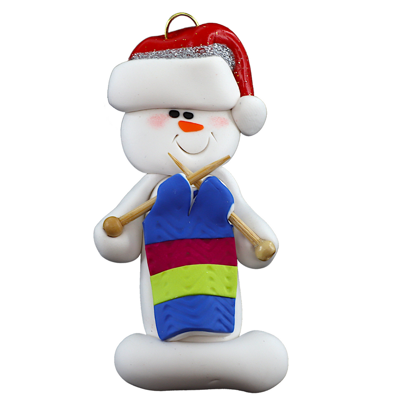 Ornament of white snowman in red hat holding an in-progress knitting project on knitting needles.