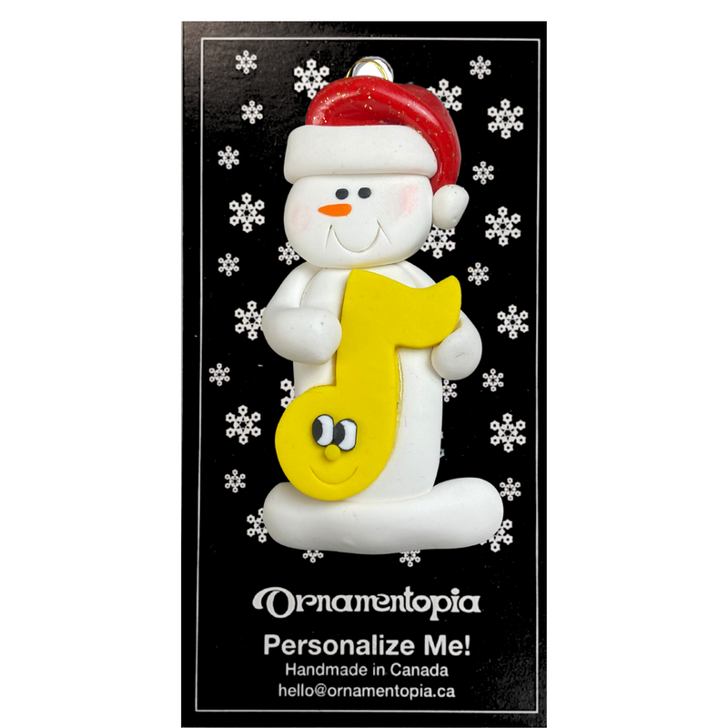 Ornament of white snowman in red hat holding a yellow music note, on display backing card.