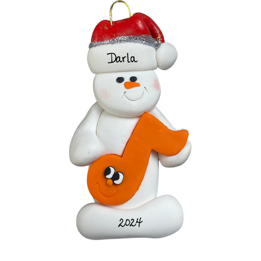 Ornament of white snowman in red hat holding an orange music note, personalized with name.