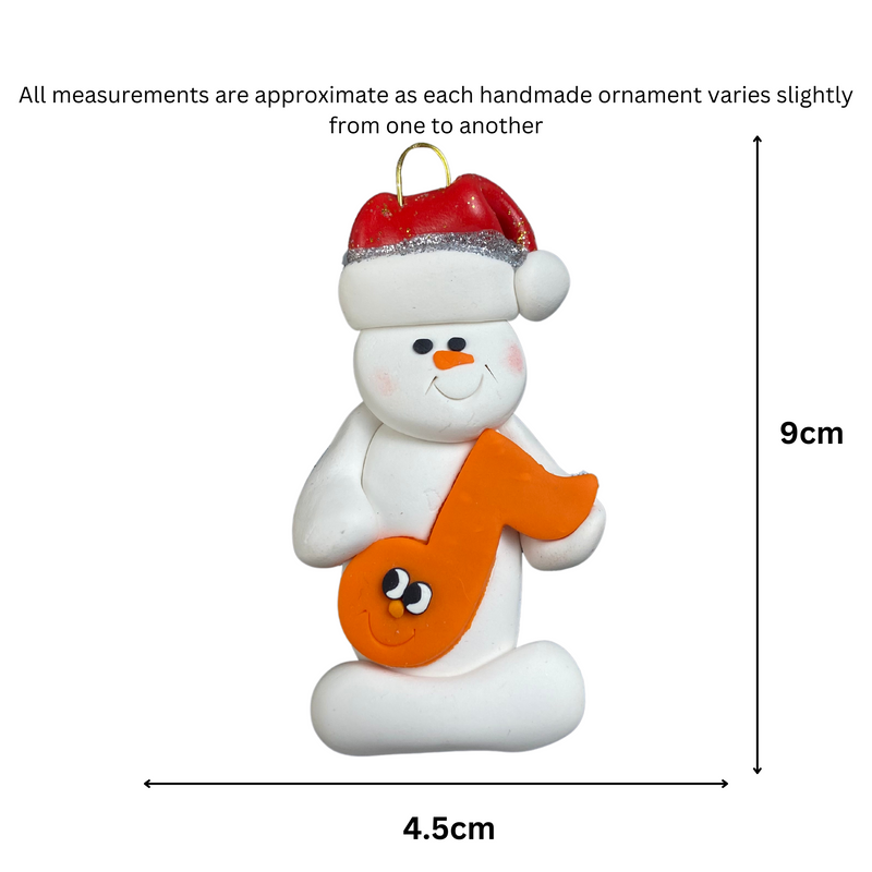 Ornament of white snowman in red hat holding an orange music note, graphed to show size (4.5x9cm).