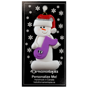 Ornament of white snowman in red hat holding a purple musical note, on display backing card.