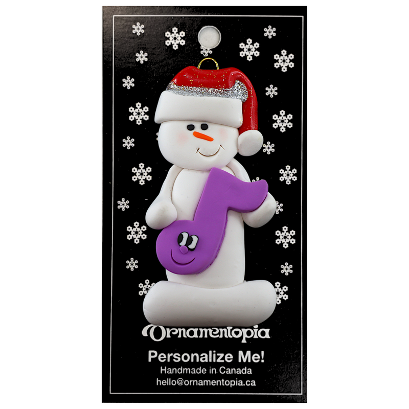 Ornament of white snowman in red hat holding a purple musical note, on display backing card.