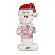 Ornament of white snowman in red hat holding a pink plastic crown, personalized with name.