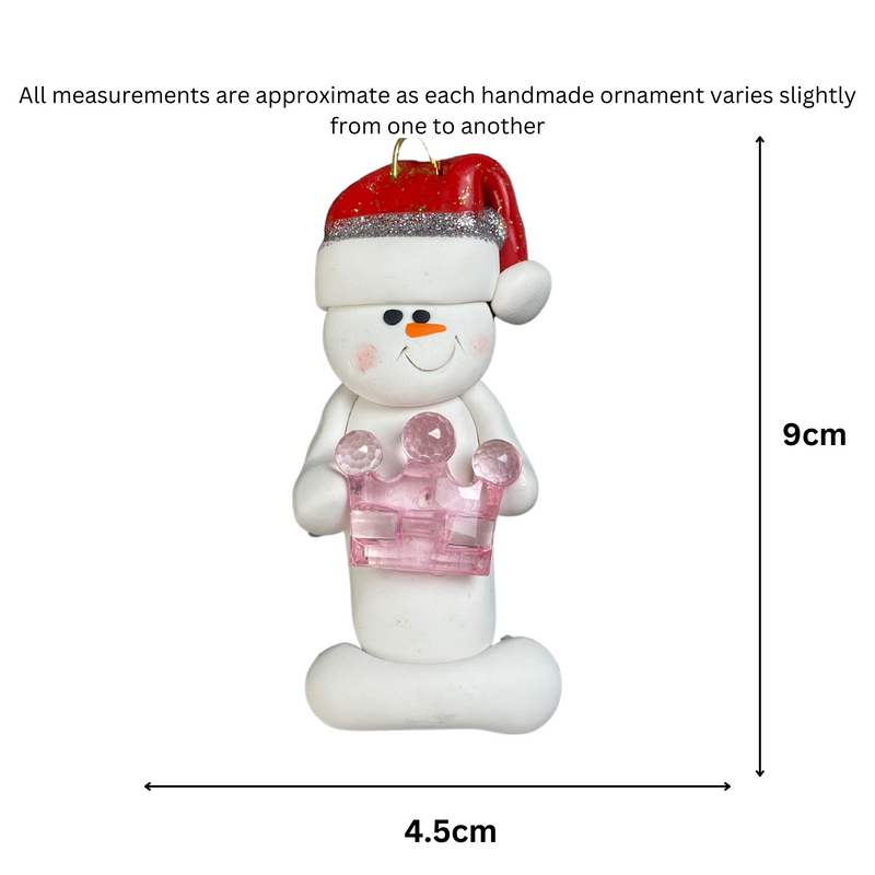 Ornament of white snowman in red hat holding a pink plastic crown, graphed to show size (4.5x9cm).