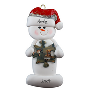 Ornament of white snowman in red hat holding a puzzle piece, personalized with name.