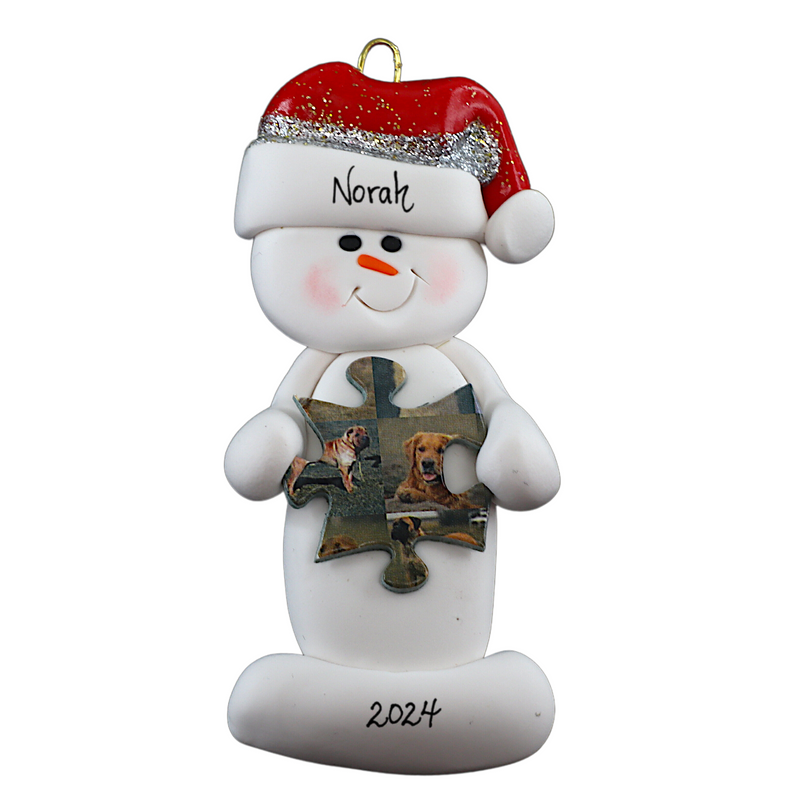 Ornament of white snowman in red hat holding a puzzle piece, personalized with name.