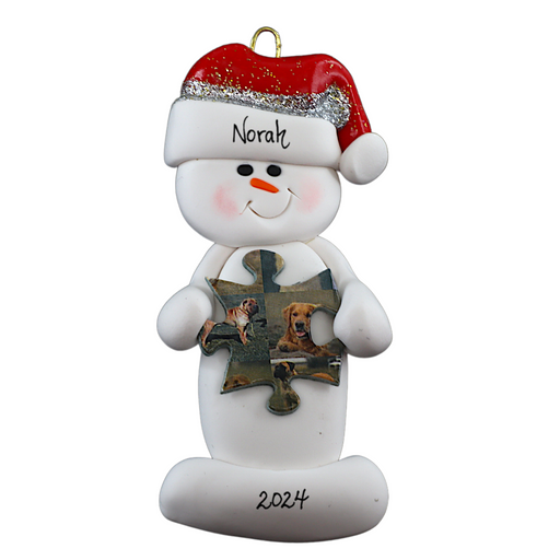 Ornament of white snowman in red hat holding a puzzle piece, personalized with name.