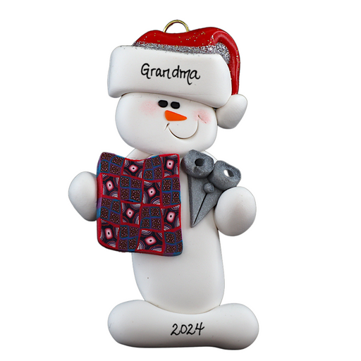 Ornament of white snowman in red hat holding a quilt block and pair of scissors, personalized with name.