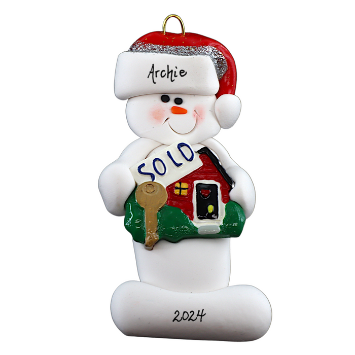 Ornament of white snowman in red hat holding a sign with a house saying “sold”, personalized with name.