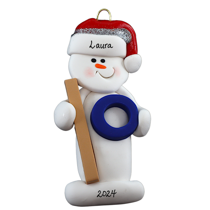 Ornament of white snowman in red hat holding a ringette stick and blue ring, personalized with name.