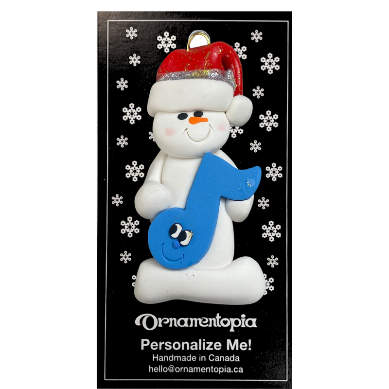 Ornament of white snowman in red hat holding a blue music note, on display backing card.